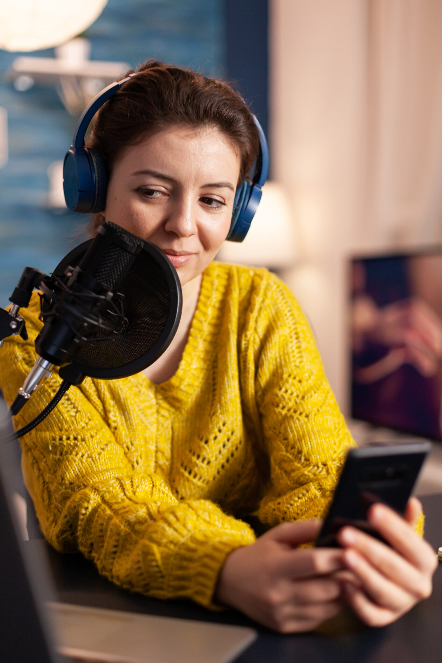 Happy blogger reading messages of fans using smartphone Happy blogger reading messages of fans using smartphone sitting in home podcast studio during livestreaming, recording. Online show On-air production internet broadcast host streaming live content.